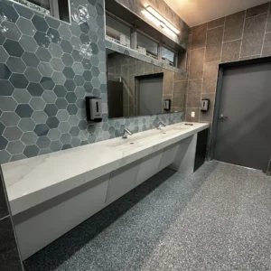 Detailed view of the sink area featuring large frameless mirrors and warm integrated lighting that highlights the textured wall tiles.