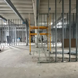 Metal stud wall partitions under construction in a commercial building with HVAC and electrical systems installed above.